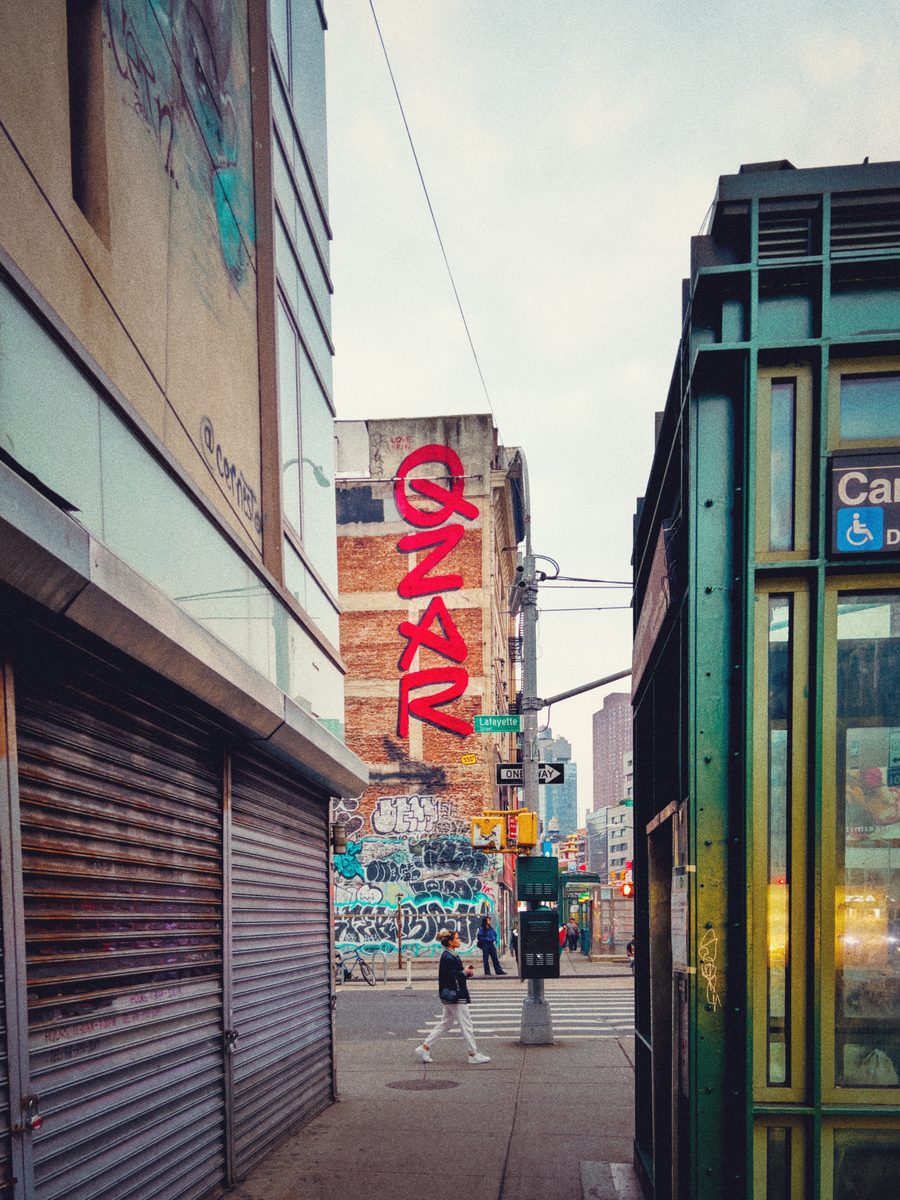 A narrow view down a Manhattan side street toward the red vertical Canal Street sign, past shuttered storefronts and graffiti.