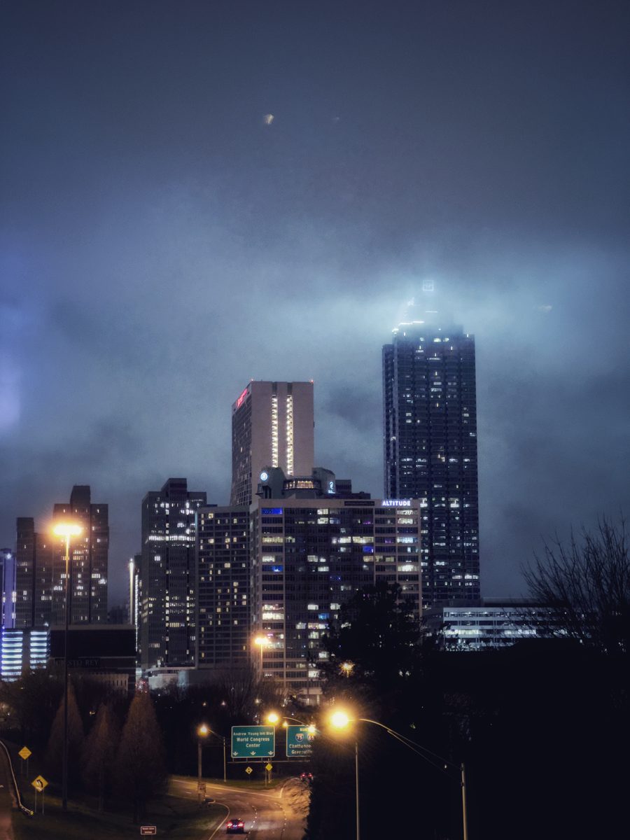 A city skyline at night with its towers disappearing into low cloud, seen from beside a lit highway.