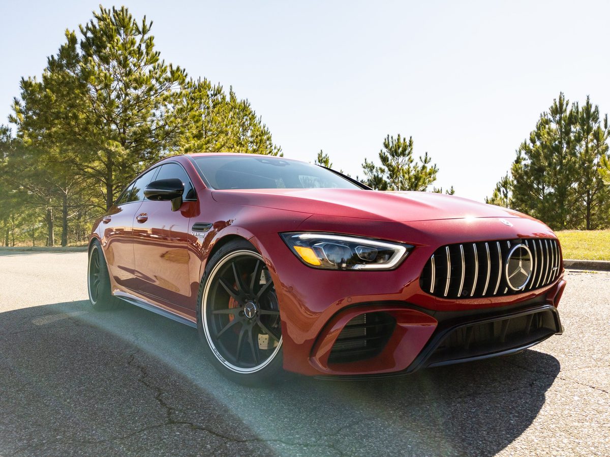 A red Mercedes-AMG GT 63 on a pine-lined road in bright hazy sunlight.