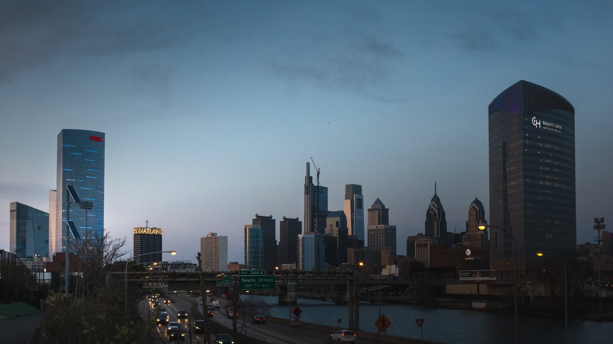 The Philadelphia skyline at dusk, seen across the interstate from a bridge with traffic below.