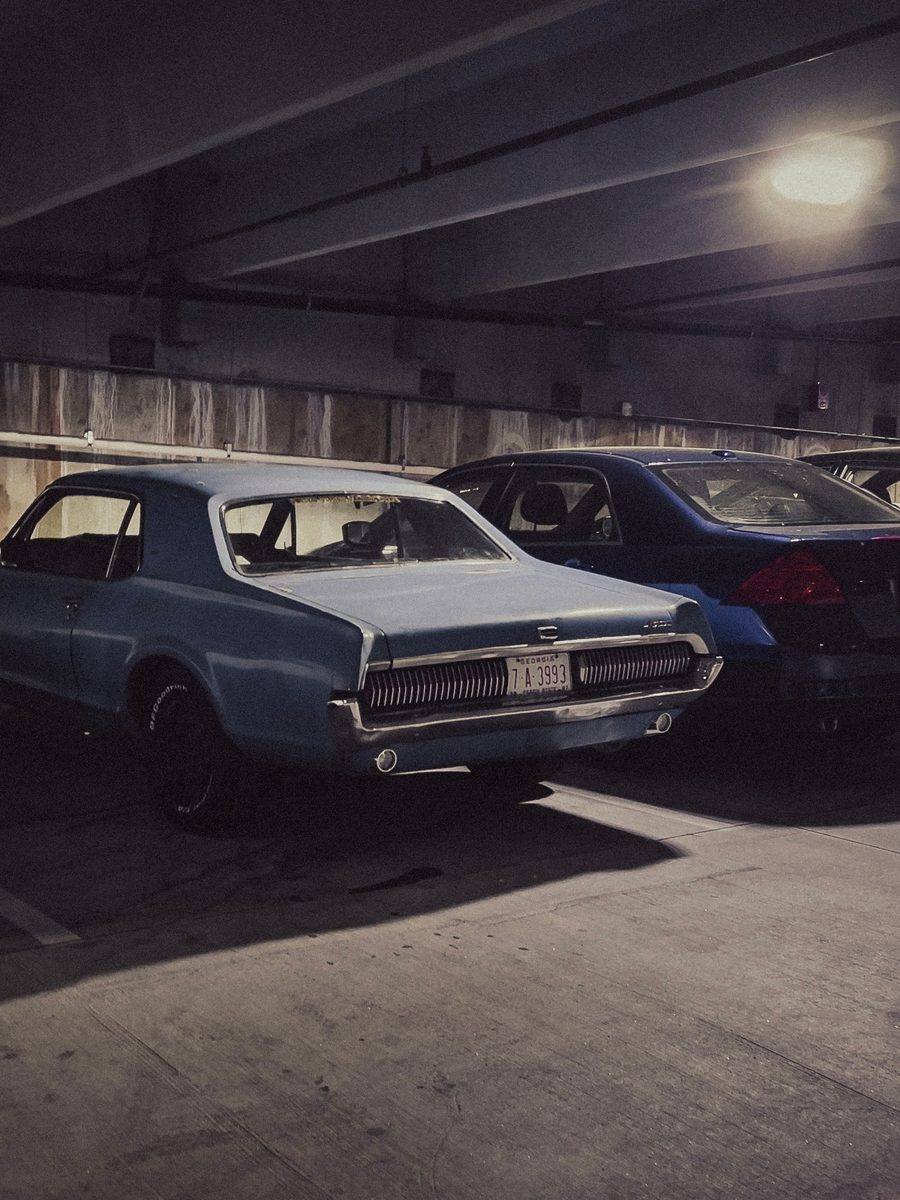 A pale blue vintage Mercury Cougar parked in a dim concrete garage under a single warm lamp.