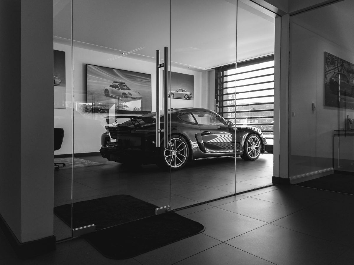 A Porsche with a fixed rear wing seen through the glass doors of a showroom, in black and white.