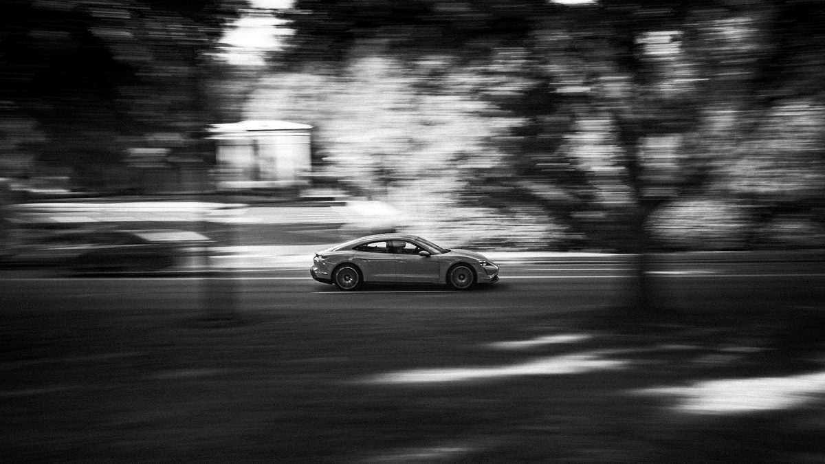 A Porsche 911 panned at speed along a tree-lined road, the background streaked into blur.