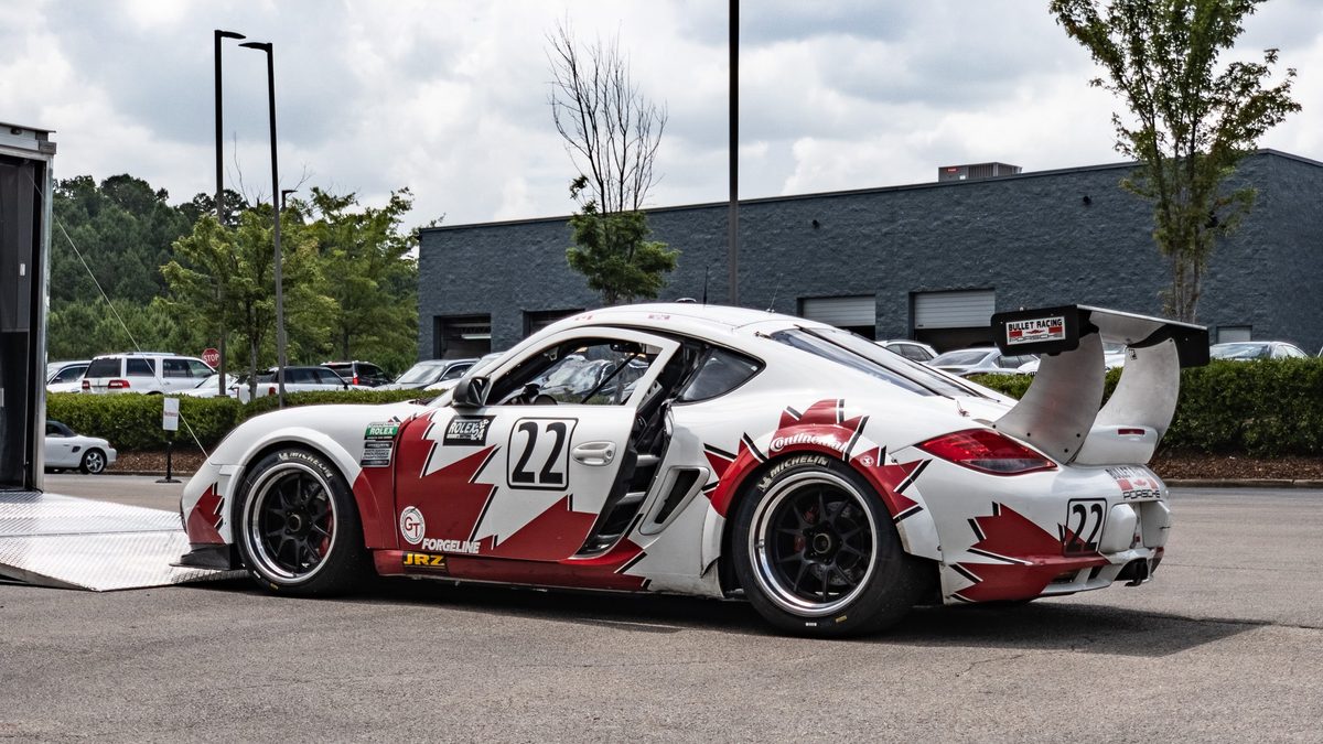 A Porsche Cayman race car in red and white number 22 livery, parked on asphalt under overcast.