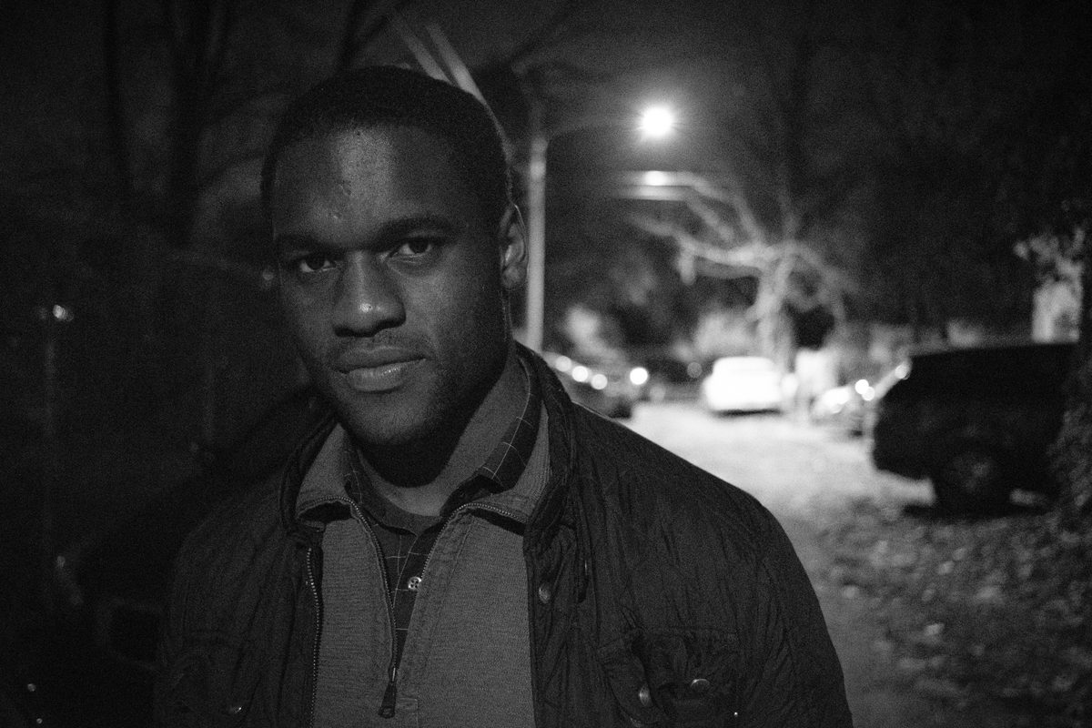 A night portrait on a residential street, lit by a streetlight, in black and white.