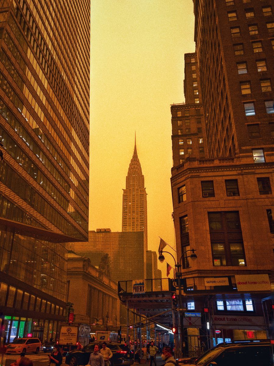 A Manhattan street looking toward the Chrysler Building under a thick orange haze.