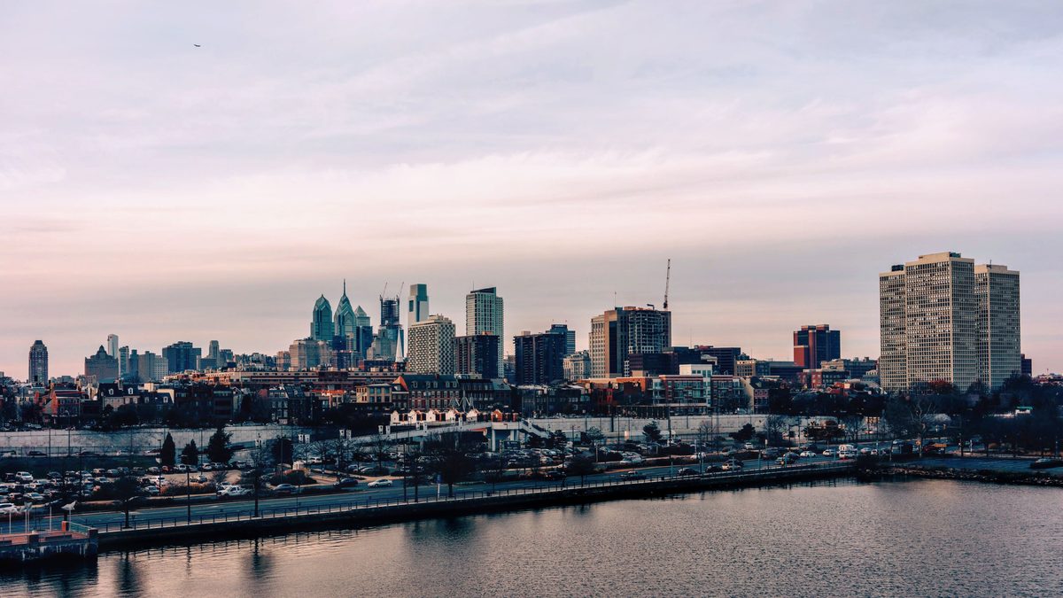 The Philadelphia skyline across the Schuylkill River at dusk under a pink sky.