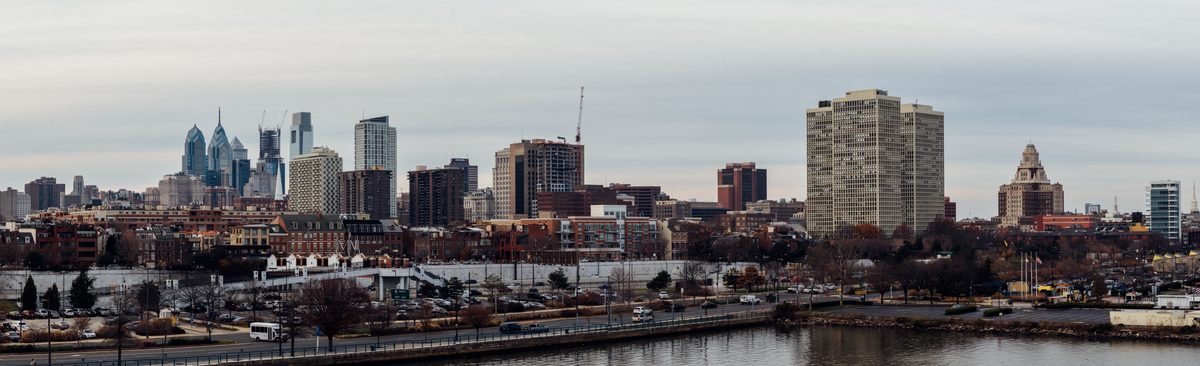 A wide panorama of the Philadelphia skyline in flat winter light, the expressway and river below.