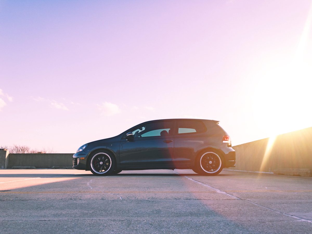 A black Volkswagen Golf GTI alone on a rooftop parking deck at sunset, the sun flaring across the frame.