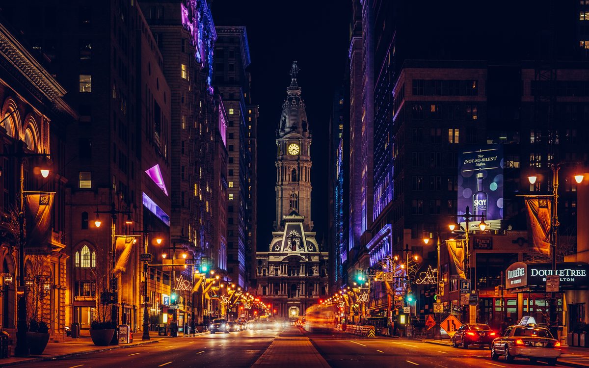 Broad Street at night looking toward the lit tower of Philadelphia City Hall, traffic trails on the road.