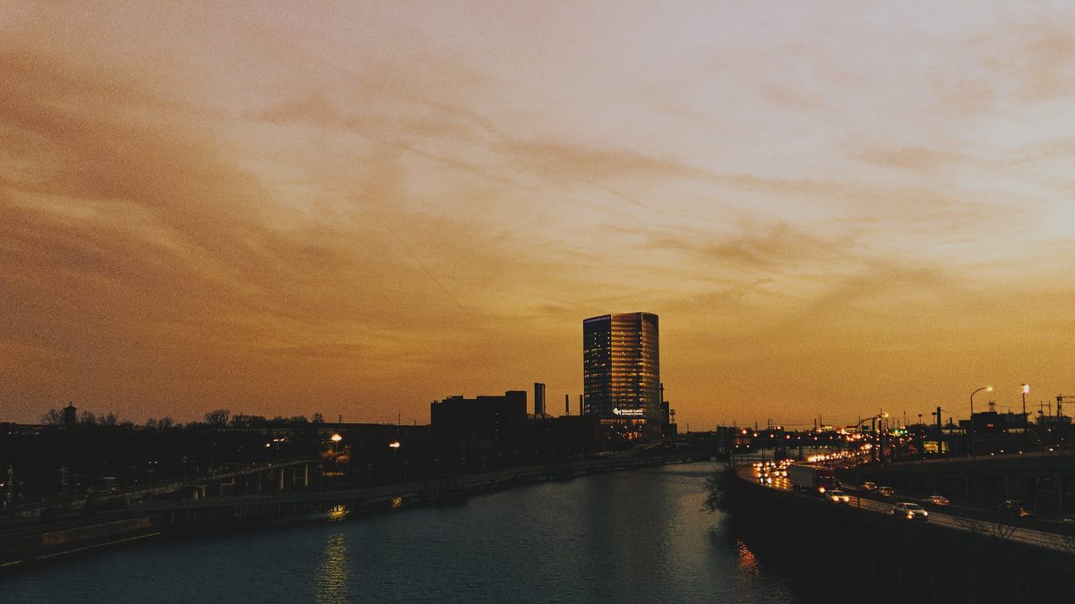 The Schuylkill at sunset, a single lit tower on the bank and headlights along the expressway.