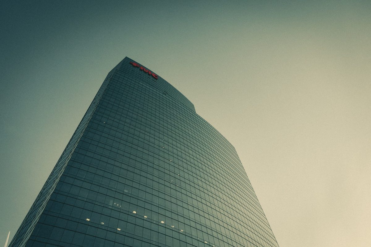 A glass tower tapering into a hazy teal sky, its sign just visible at the crown.