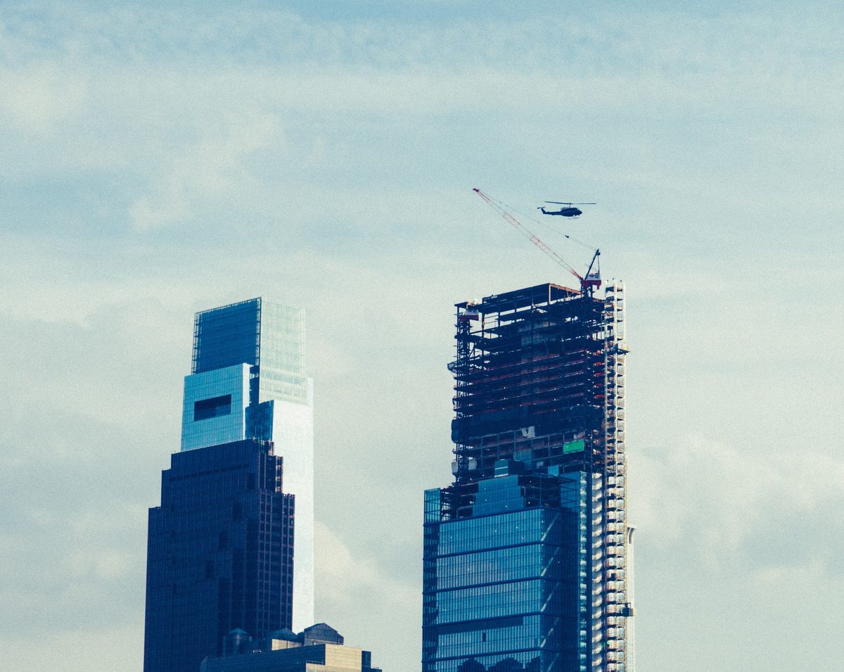 Two Philadelphia towers, one still under construction with its crane, a helicopter passing above.