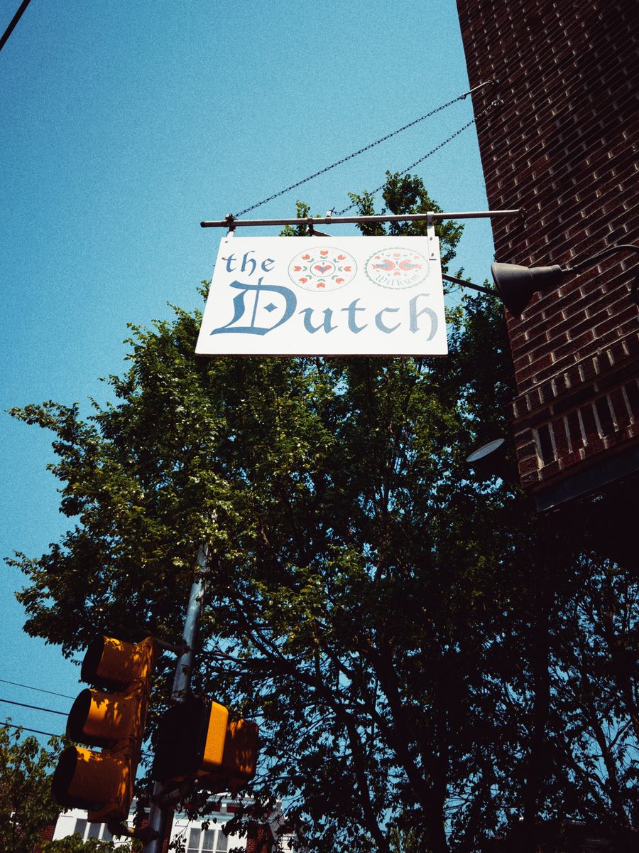 A hanging sign reading the Dutch against a deep blue summer sky, traffic lights below.