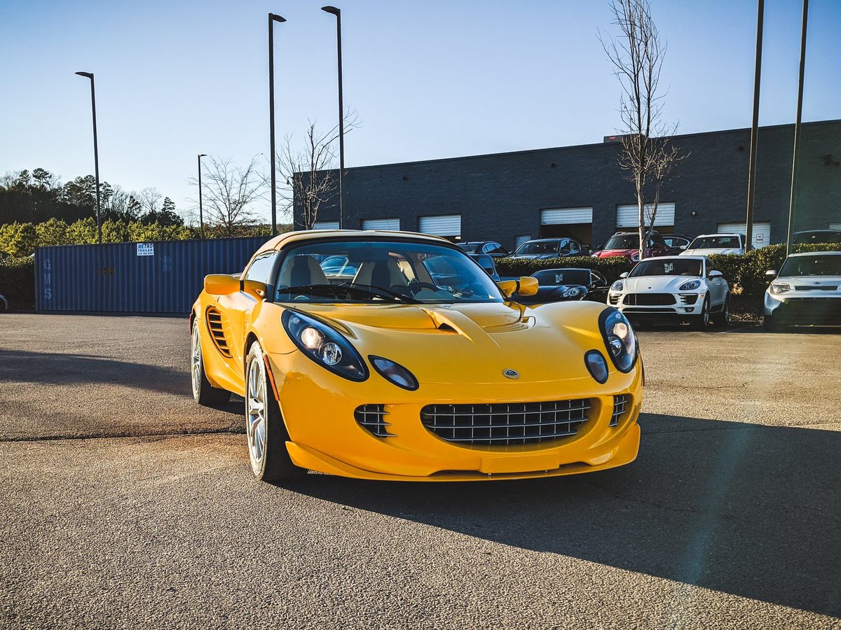 A yellow Lotus Elise parked in a lot in low winter sun, long shadows across the asphalt.