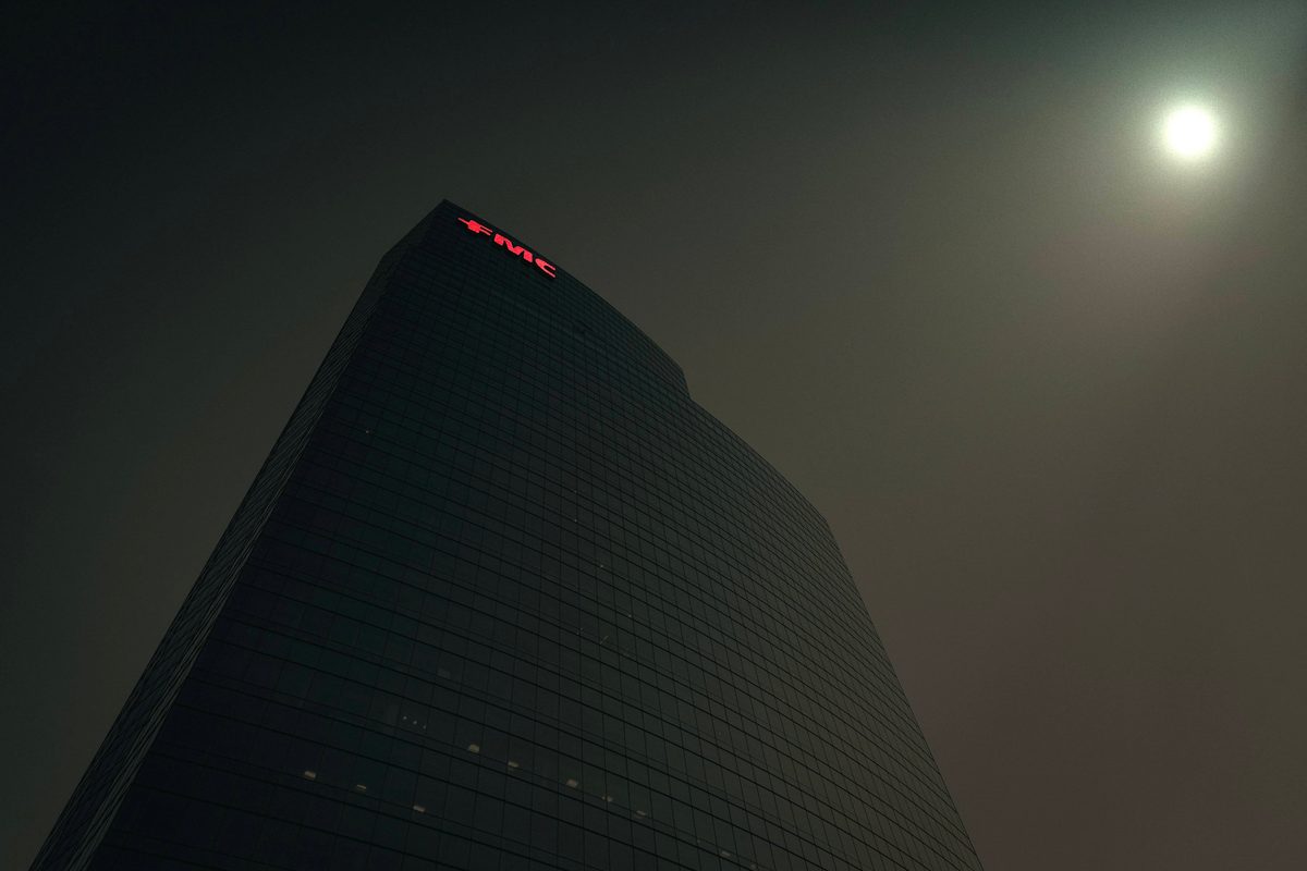 A glass tower at night in thick haze, its rooftop sign lit and the moon burning through the murk.