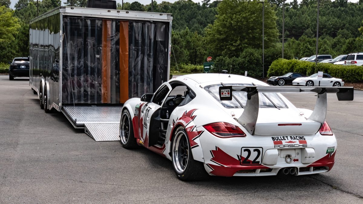 A number 22 Porsche Cayman race car parked at the ramp of its enclosed trailer.