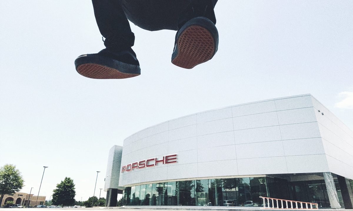 Someone jumping over the camera outside a Porsche dealership, the soles of their shoes filling the top of the frame.