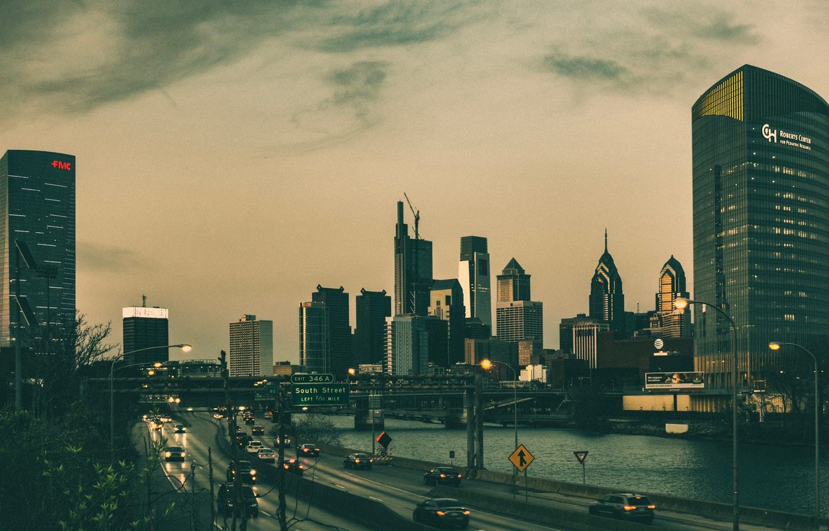 The Philadelphia skyline at dusk above the expressway, seen from a bridge with traffic beneath.