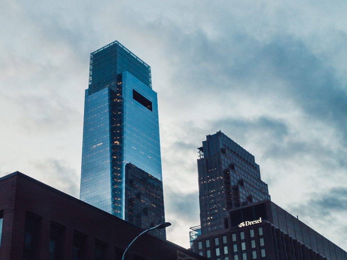 A blue glass tower and its neighbours under heavy dusk cloud, a Drexel sign on the rooftop below.