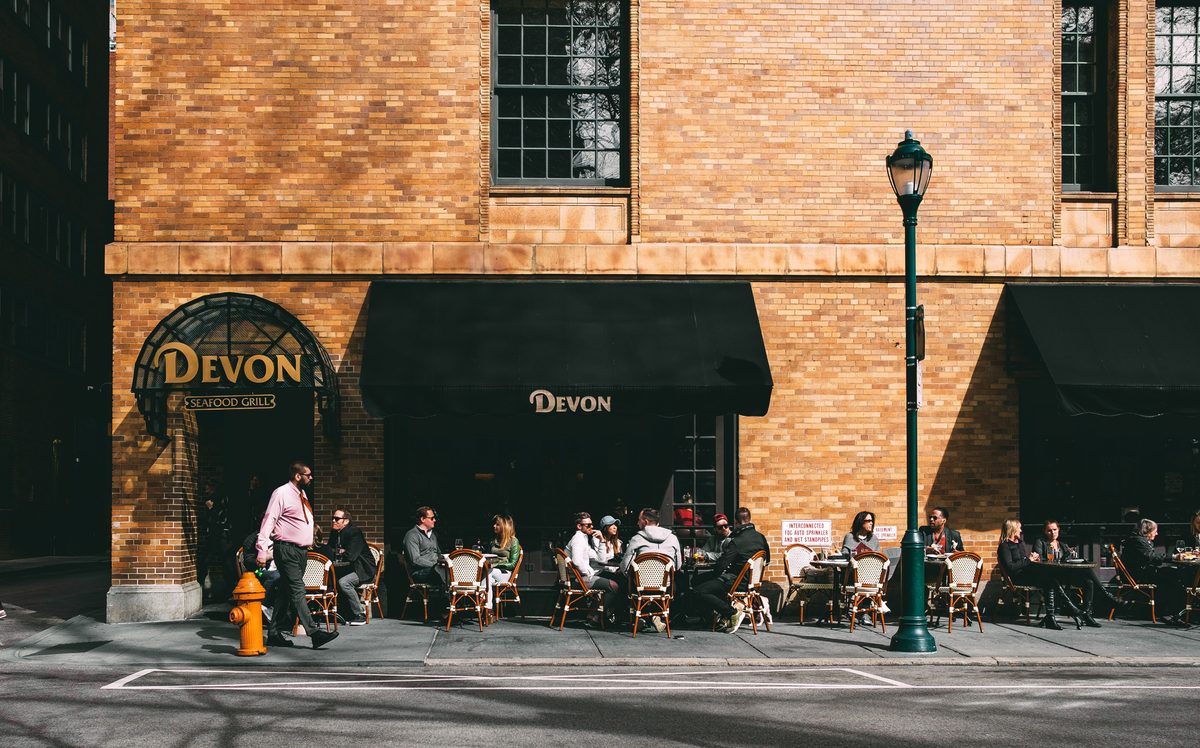 Diners at pavement tables outside the brick frontage of the Devon Seafood Grill in spring sun.