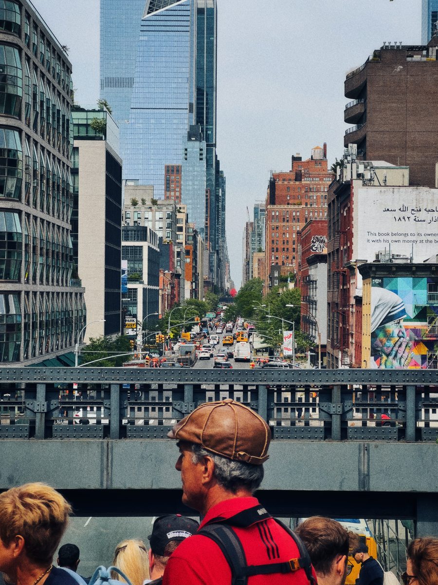 Looking down a Manhattan avenue from the High Line over the heads of the crowd, a mural on the wall at right.