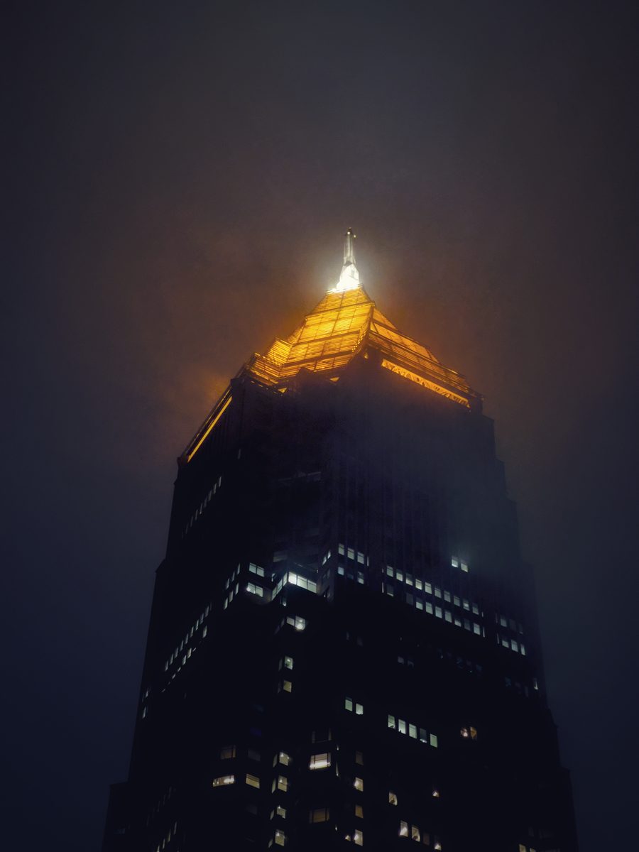 The lit crown and spire of a skyscraper glowing through night fog.