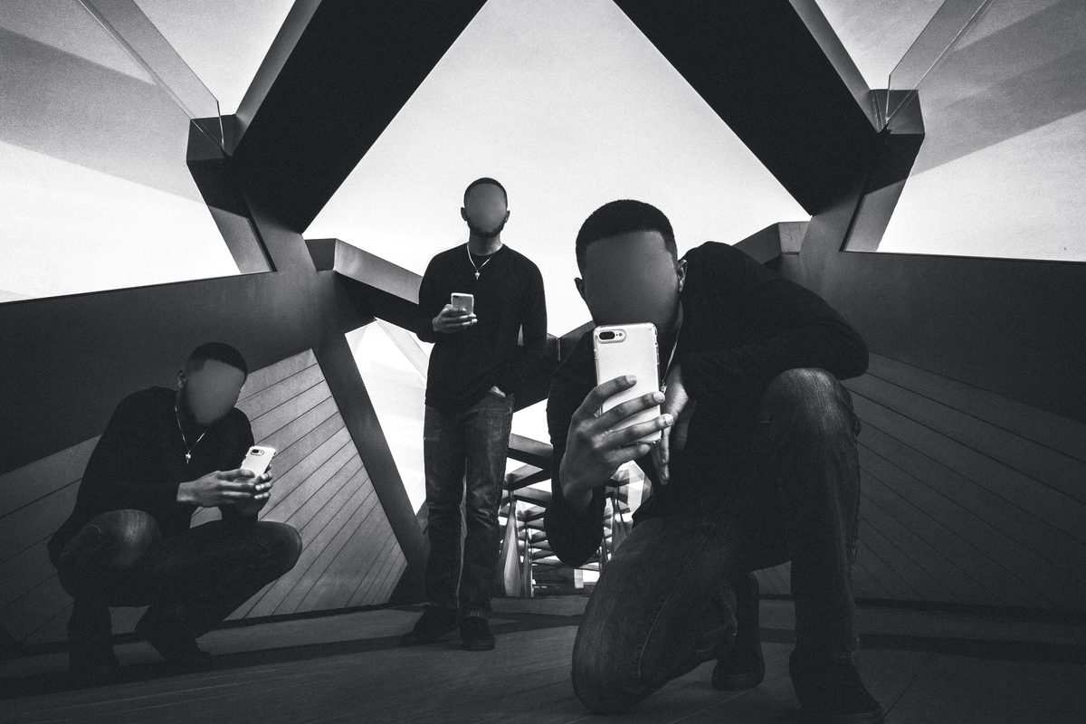 Three men on their phones inside an angular steel pavilion, faces left blank, in black and white.