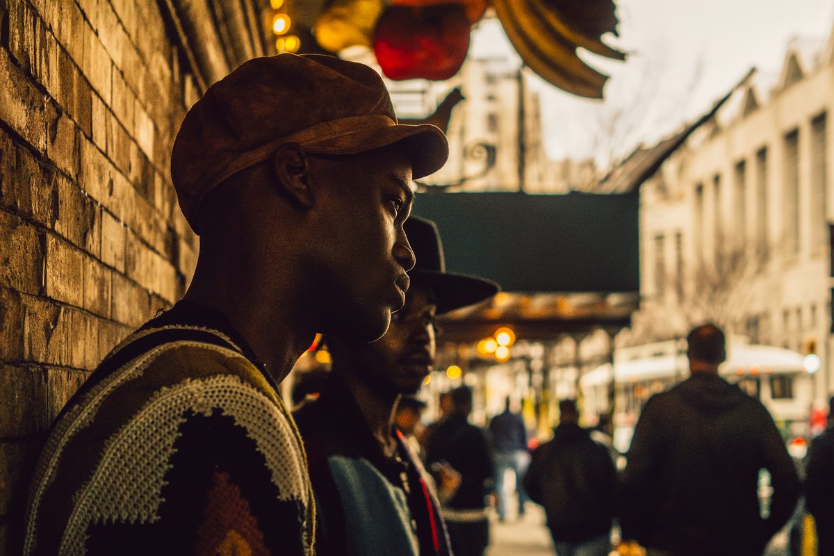 Two men in caps against a brick wall in warm late light, a busy street falling away behind them.