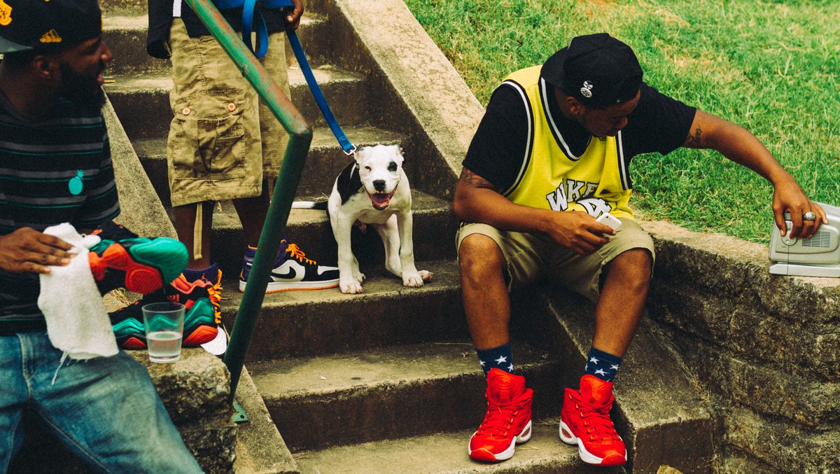 Men sitting on concrete steps in summer with a puppy between them, a radio at one elbow.