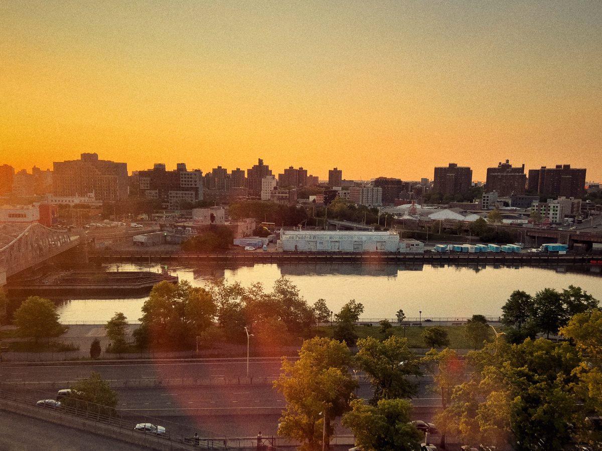 A river at sunset below a low skyline, the sky burning orange over rail yards and trees.