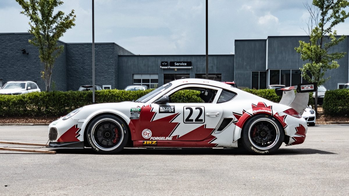 A number 22 Porsche Cayman race car in profile outside a service building.