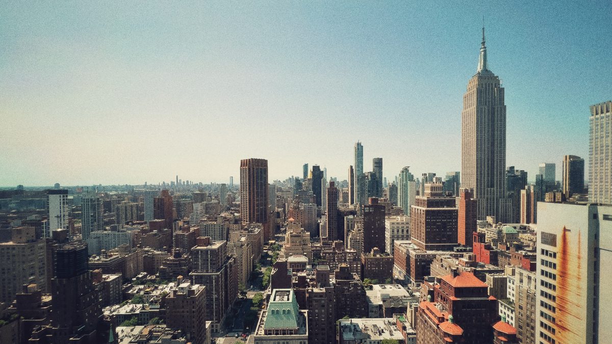 Midtown Manhattan from above, the Empire State Building standing over the rooftops in clear summer light.