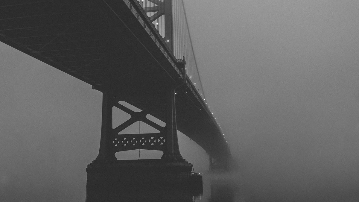 The Benjamin Franklin Bridge disappearing into fog, its tower and cables fading out, in black and white.