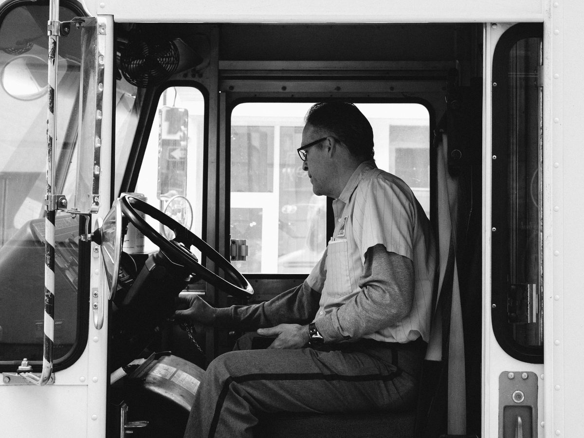 A delivery driver at the wheel of his truck, seen through the open door, in black and white.