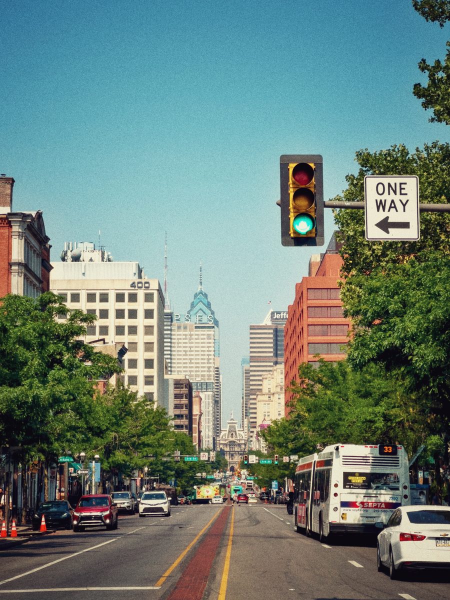 Broad Street looking toward City Hall in summer, a SEPTA bus at the kerb under a one-way sign.
