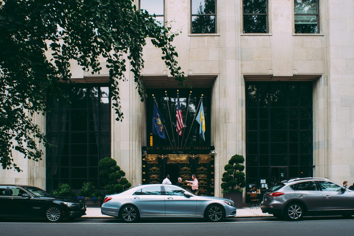 The stone entrance of 210 West Washington Square, cars at the kerb and doormen on the pavement.