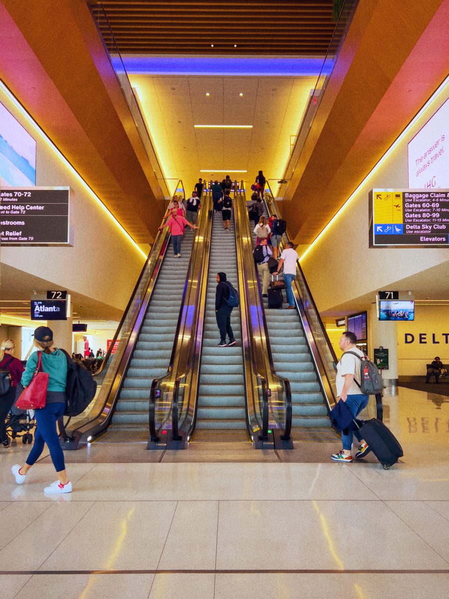 Travellers on the escalators of an airport terminal under coloured cove lighting.