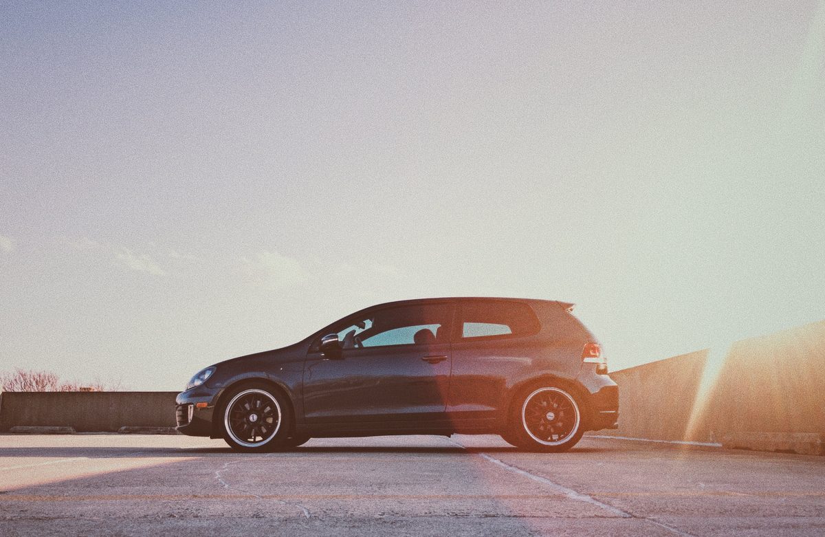 A black Volkswagen Golf GTI in profile on a rooftop deck, the sun low and flaring off the parapet.