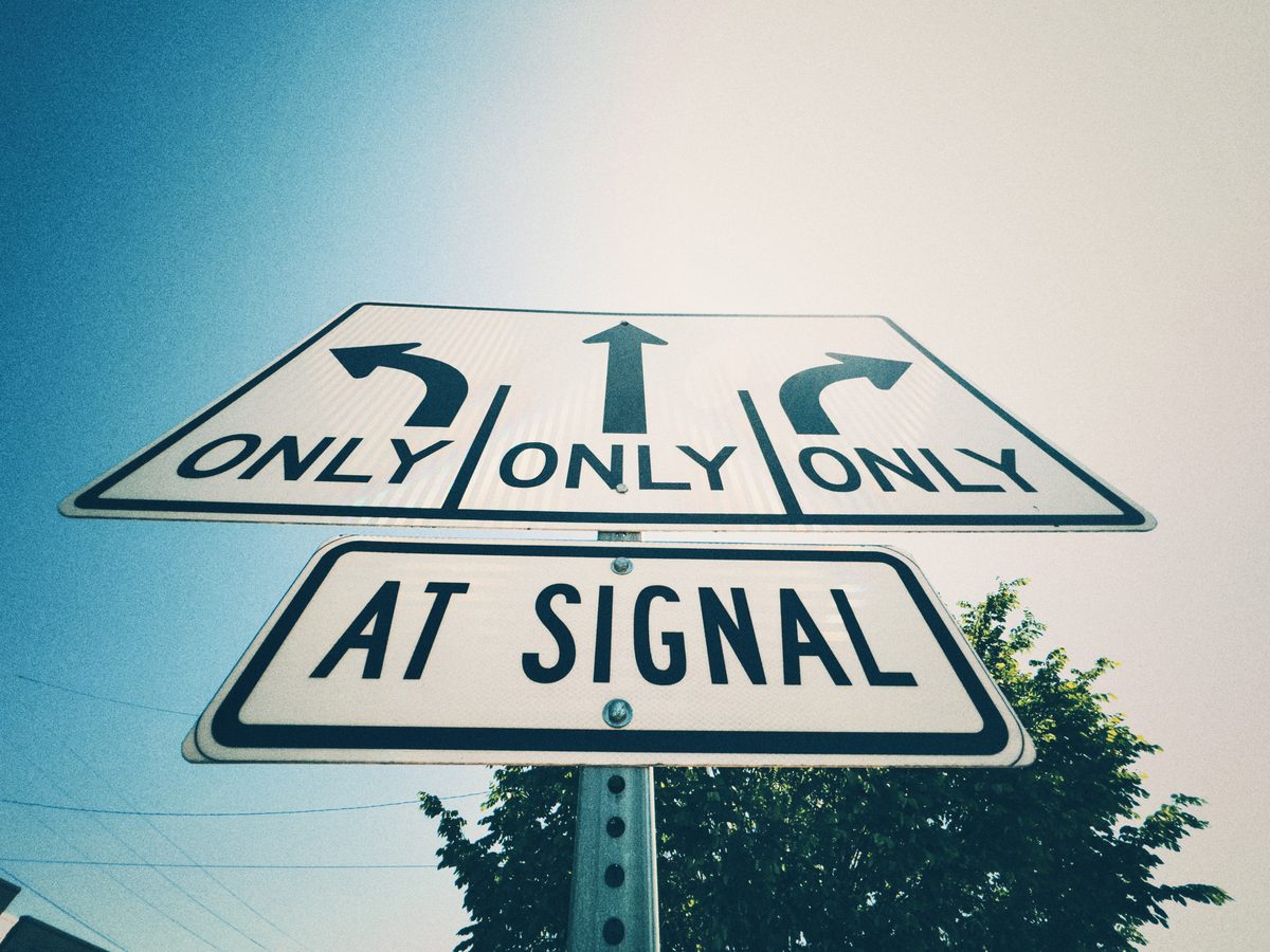 Stacked lane-direction signs reading Only, Only, Only above At Signal, shot from below against a pale sky.